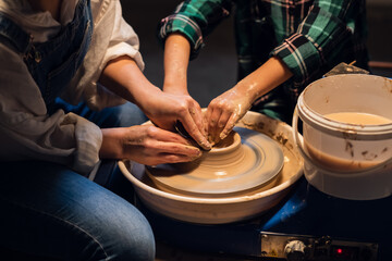 a young female potter teaches a small boy to make a pot of clay