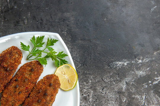 top half view cutlets lemon slices parsley and black pepper on white plate on grey background with free space