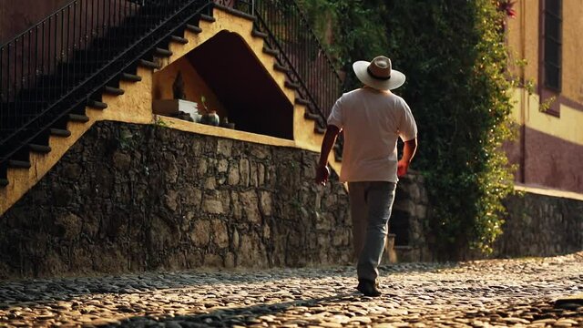 Surface level rear view of man walking on sunny cobblestone street