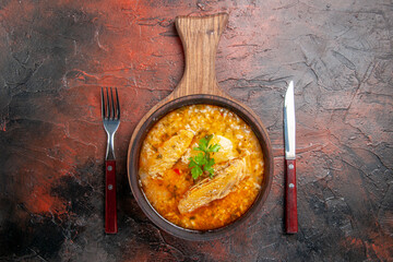 top view chicken soup in wooden bowl with handle fork and knife on dark red background with copy space