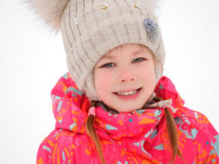 Cute child girl playing on a winter walk in nature. A close up portrait of a little pretty charming smiling girl in a knitted hat in a frosty winter day outdoor.