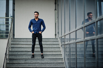 Middle eastern entrepreneur wear blue shirt, eyeglasses against office building.