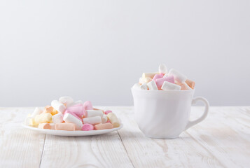 Fototapeta na wymiar white cup with marshmallows and white saucer with marshmallows on a white wooden table