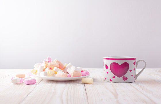 cup with a picture of a heart and a saucer with marshmallows on a white wooden table