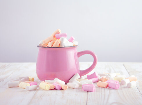 pink cup with marshmallows and marshmallows scattered around it on the  table