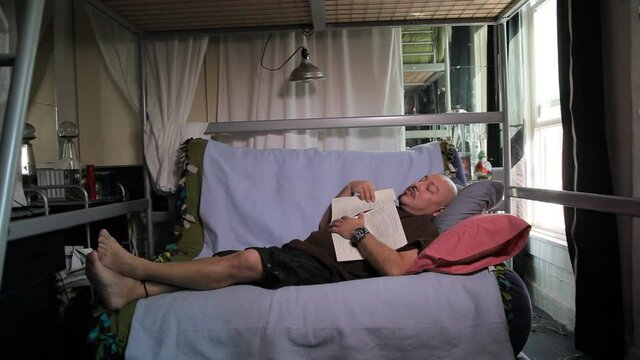 Middle-aged man reading paperwork then napping on futon