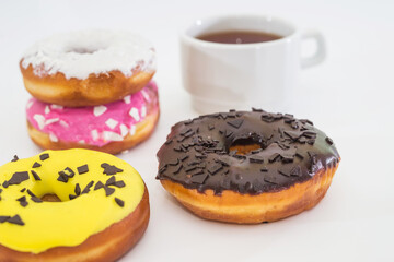 cup of tea and traditional american donuts with chocolate, pink, yellow, white icing and sprinkles on white