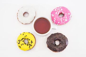 cup of tea and traditional American donuts with chocolate, pink, yellow, white icing and sprinkles on a white background.