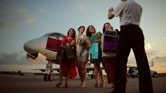 Pilot photographing women with shopping bags on tarmac near private jet