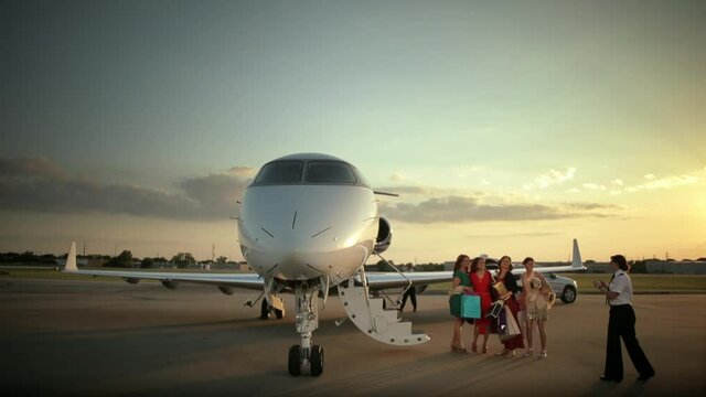 Pilot photographing women with shopping bags on tarmac near private jet