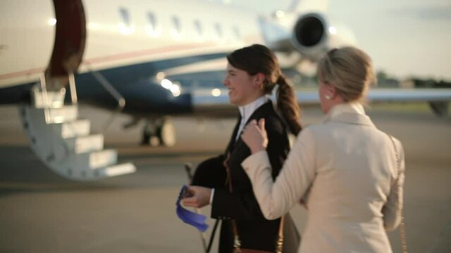 Caucasian girl showing first place ribbon to grandmother near private jet