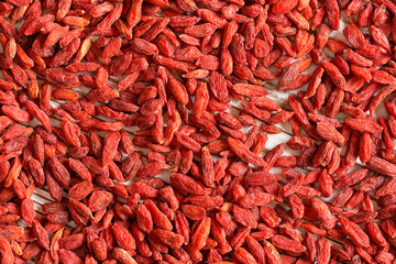Fototapeta premium Detail closeup photo of goji berry (wolfberry - Lycium chinense) dried fruits heap shot from above, white wooed board visible under