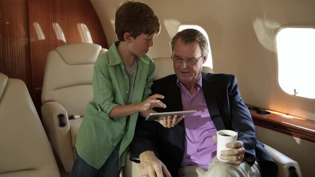 Caucasian boy showing digital tablet to grandfather on private jet