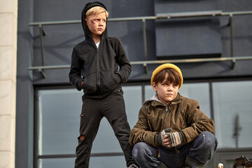 lonely street children in dirty wear spend time together outdoors, sitting on trash cans, rubbish