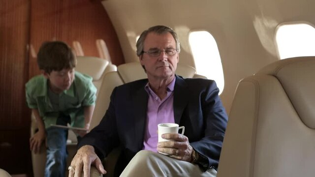 Caucasian boy showing digital tablet to grandfather on private jet