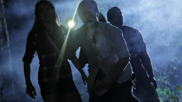 Cautious friends walking in woods at night with flashlights