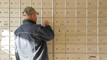 Middle-aged man retrieving mail from apartment mailbox wall
