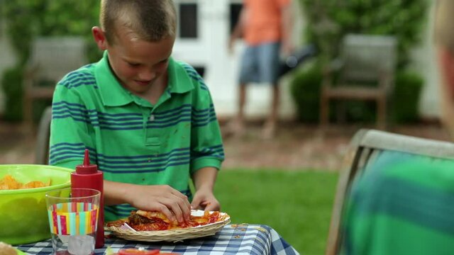 Caucasian boy slamming top of bun onto messy cheeseburger
