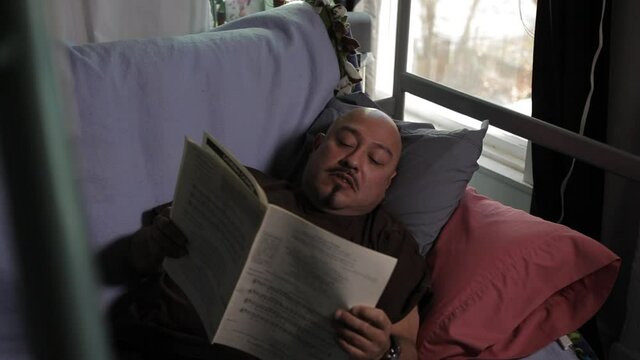 Middle-aged man laying on futon reading paperwork