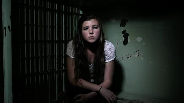 Caucasian teenage girl sitting in dark jail cell