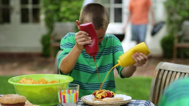 Caucasian boy dousing cheeseburger with mustard and ketchup
