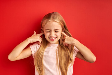 child girl closing her ears, doesn't listen to talks. isolated red background