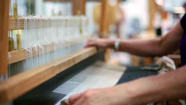 Close up of hands of woman pulling loom to weave fabric