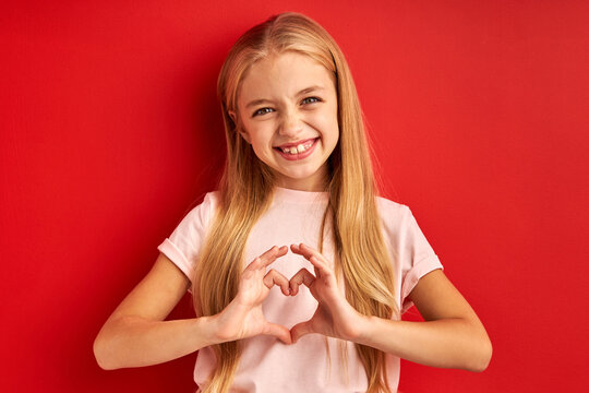 happy girl with long hair make love gesture at camera, expresses love. isolated on red background