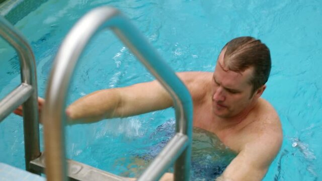 Caucasian man swimming to ladder then exiting pool