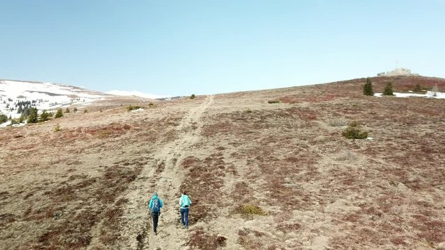A drone capture of a couple with big backpacks hiking to Seiner Kreuz, a peak in Austrian Alps. Cross on the peak. There are a few snow fields around. Early spring in the mountains. Wanderlust
