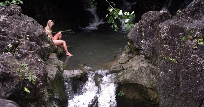Caucasian woman crossing waterfall in the forest of Maui