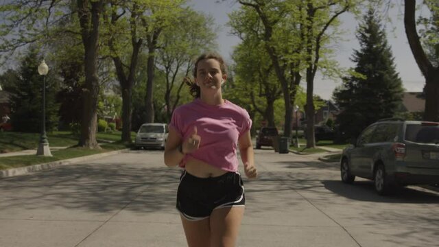 Tracking shot of teenage girl jogging in neighborhood street / Salt Lake City, Utah, United States