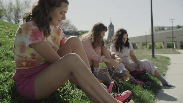 Slow motion of girls sitting in grass tying shoelaces on roller skates / Salt Lake City, Utah, United States