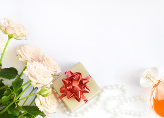 Fototapeta na wymiar Gift box with red bow, pink roses, beads with perfume bottle on white background