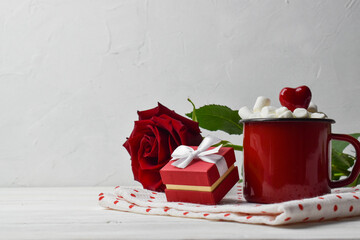 Holiday card for Valentine's Day. Red mug with marshmallows on a napkin with a gift box and a red rose.