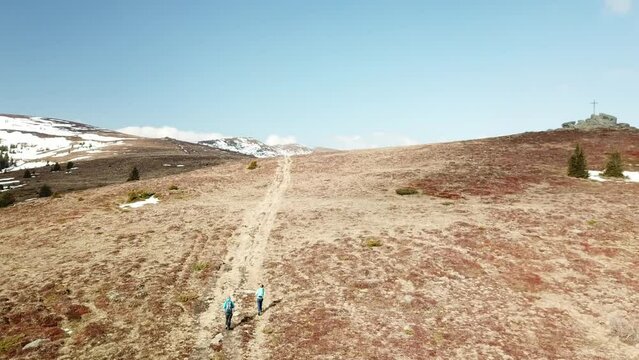 A drone capture of a couple with big backpacks hiking to Seiner Kreuz, a peak in Austrian Alps. Cross on the peak. There are a few snow fields around. Early spring in the mountains. Wanderlust
