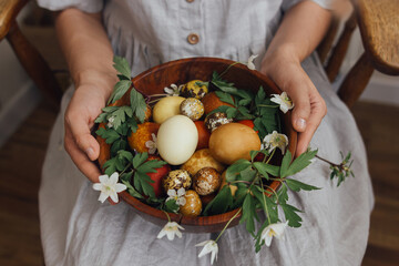 Happy Easter! Easter eggs and spring flowers in wooden bowl in hands. Aesthetic holiday