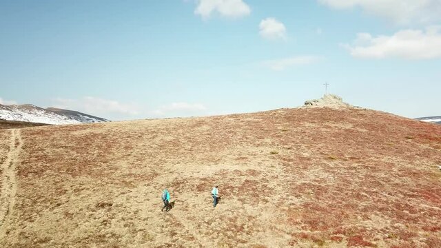 A drone capture of a couple with big backpacks hiking to Seiner Kreuz, a peak in Austrian Alps. Cross on the peak. There are a few snow fields around. Early spring in the mountains. Wanderlust
