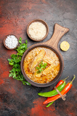 top view chicken soup on chopping board parsley a bowl of rice sea salt lemon slice hot peppers on dark red background