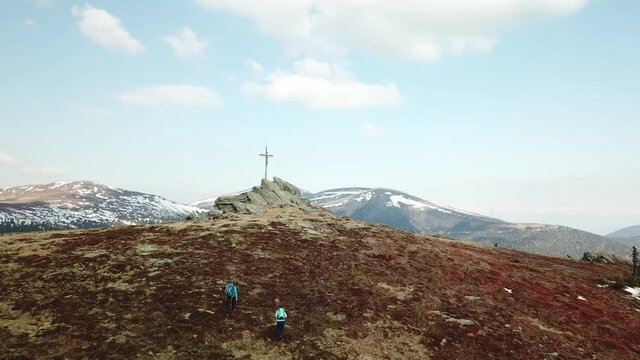 A drone capture of a couple with big backpacks hiking to Seiner Kreuz, a peak in Austrian Alps. Cross on the peak. There are a few snow fields around. Early spring in the mountains. Wanderlust
