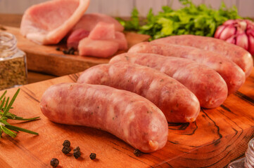 Brazilian pork leg sausage on wood cutting board with pork leg in background - Linguiça de pernil close up