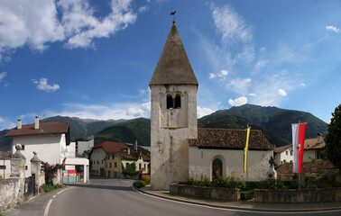 Fototapeta na wymiar Street with the romanesque church of St Nikolaus in Latsch village, Vinschgau region in South Tyrol, Italy