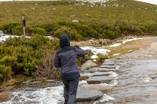 Horizontal view of a woman jumping between some stones in order to cross a river