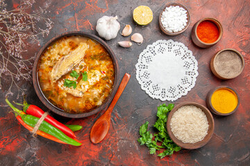 top view homemade chicken and rice soup in a bowl wooden spoon bowl of rice garlic slice of lemon parsley leaves hot peppers different spices white lace doily on dark red background