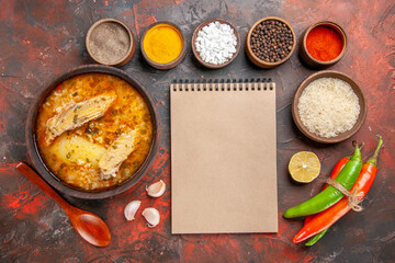 top view bowl of chicken soup bowls with different spices wooden spoon bowl of rice hot peppers a notebook on dark red background