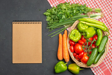 Above view of fresh various organic vegetables in a wooden basket on orange stripped towel and notebook on dark background