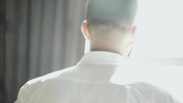Back view of handsome man puts oa white shirt