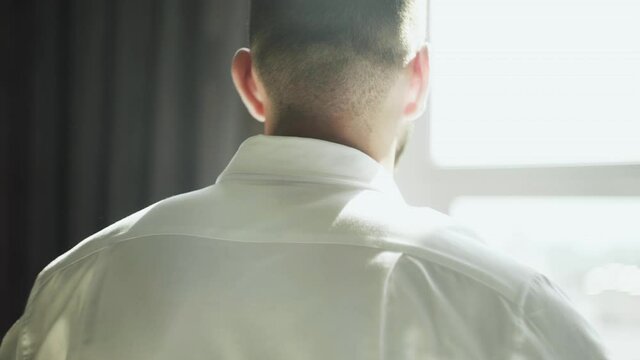 Back view of handsome man puts oa white shirt