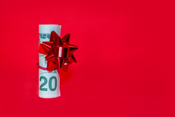 A wad of US dollar bills wrapped in a red ribbon with a gift bow attached on red background.