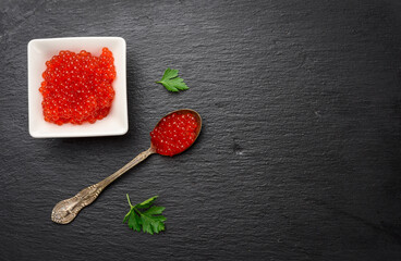 fresh grained red chum salmon caviar in a white ceramic bowl on a black slate stone background